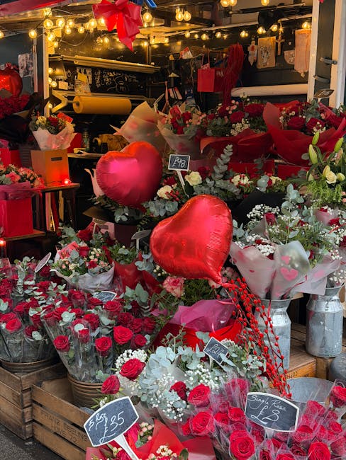 A vibrant display of fresh flowers arranged on a flower stall at Flowers Hampstead Garden Suburb. The arrangement features red roses, white lilies, and small white flowers, complemented by green folia