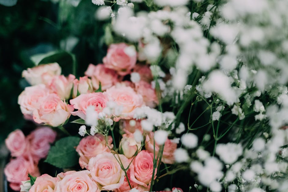 A close-up view of a floral arrangement featuring soft pink roses with lush, layered petals and green stems, complemented by delicate white baby's breath flowers on thin, branching stems. The roses ar